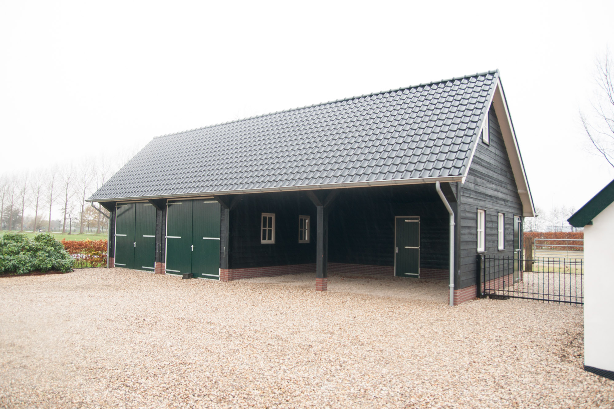 Grote houten zwarte schuur met dubbele deuren en carports